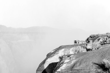 Tourists are drenched by the spray of falling water at a viewpoint at the Augrabies waterfalls in the Orange River. The river is in flood. Monochromeの写真素材