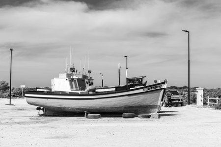Struisbaai, South Africa - Sep 21, 2022: Fishing boats at the harbor in Struisbaai, in the Western Cape Province. People are visible. Monochromeのeditorial素材