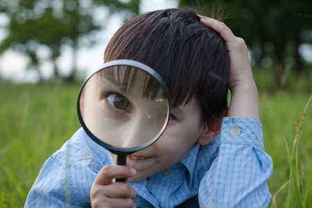 Boy with magnifying glass lying on the grassの写真素材