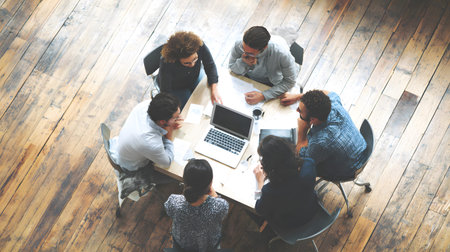 Group of professionals working together in an office top view, collaborating around a laptop during...