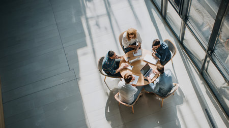 Group of professionals working together in an office top view, collaborating around a laptop during...