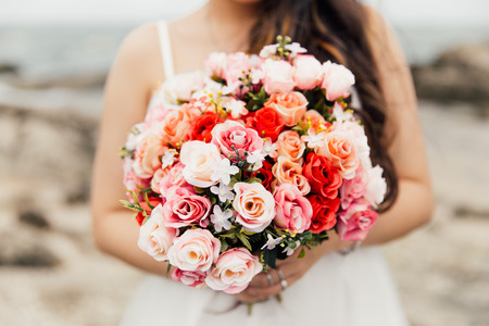 A  beautiful rose bouquet in bride hands on the sea backgroundの写真素材
