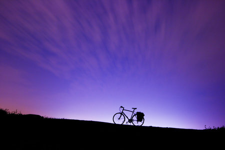 Silhouette of a bicycle on a hill at night with a large sky