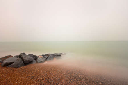 Rocks on a pebble beach plain overcast sky and long exposureの写真素材