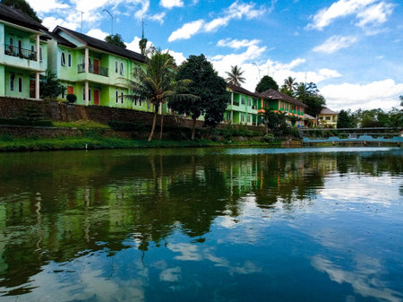 Peaceful tropical village with colorful houses reflected in calm river under blue sky.の写真素材