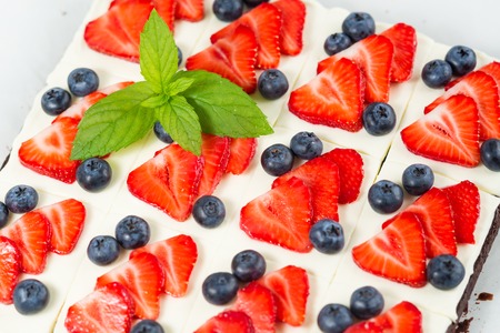 Pieces of chocolate cake with icing, strawberry, blueberry and mint on a plateの写真素材