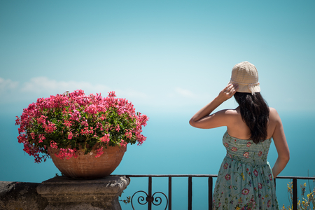A young girl in a sun-hat near blossom flowers staying at the sea coast and looking forward to the horizonの写真素材