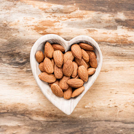 Almonds in a wooden saucer on a natural wooden background.の写真素材
