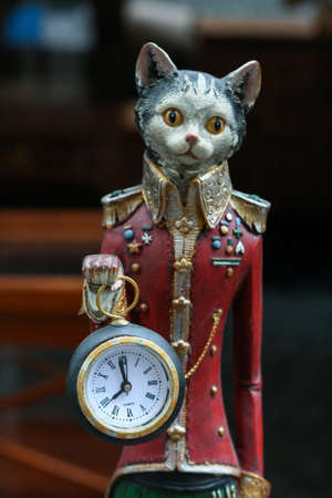Statuette of a long sad cat in a red coat holding a clockの写真素材