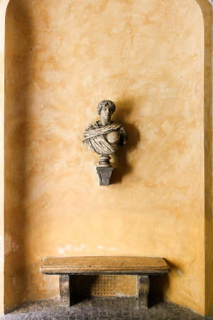 Antique Roman bust, stone bench and a yellow orange stucco wall.の写真素材