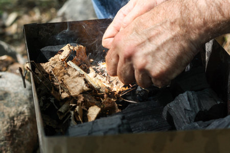 A man lights a fire with a flint. Coal, bright sparkles with smoky tails, dry leaves and twigs.