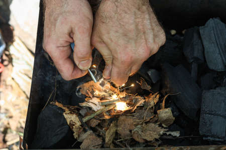 A man lights a fire with a flint. Coal, bright sparkles with smoky tails, dry leaves and twigs.の写真素材
