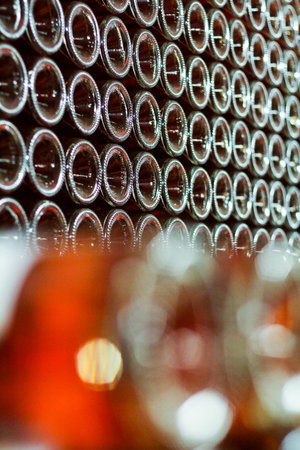 Lots of rose wine bottles stacked. Watching from the bottoms. Part of the frame strongly blurred.