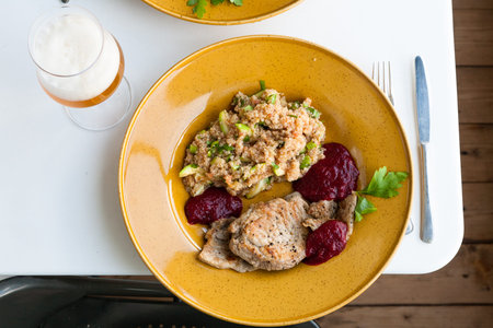 Pork grilled with a side dish of quinoa and grilled zucchini with cranberry sauce on a large yellow plate on white table. Glass of beer with foam head. Dostchaty floor.の写真素材