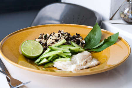 Baked cod with rice and mushrooms of Moher in the Chinese style. Half a lime and basil. Large yellow plate and white table.の写真素材