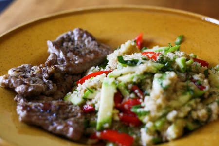 Pork grilled with a side dish of quinoa and grilled vegetables - zucchini and peppers on a large yellow plate.の写真素材