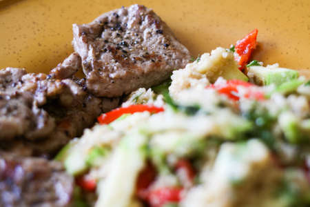 Pork grilled with a side dish of quinoa and grilled vegetables - zucchini and peppers on a large yellow plate.の写真素材