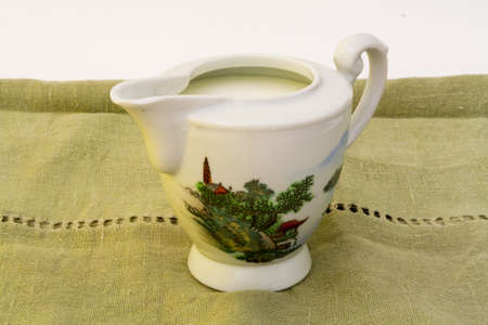 Antique milk jug with a Japanese painting on green linen tablecloth.の写真素材