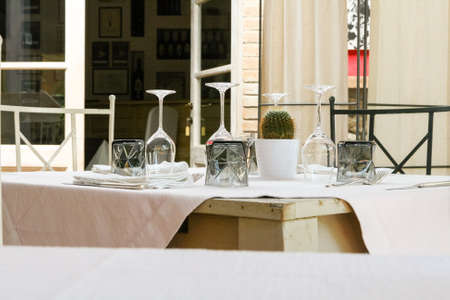 Square wooden table with linen cloth on which glasses and cutlery.の写真素材