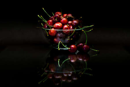 Transparent cup with red ripe cherries with reflection on black background.の写真素材