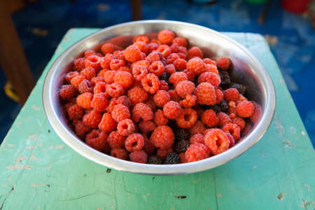Metal bowl with raspberries on old turquoise stool.の写真素材