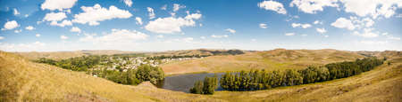 Summer panorama of the hilly terrain of the steppe lake, trees and village.の写真素材