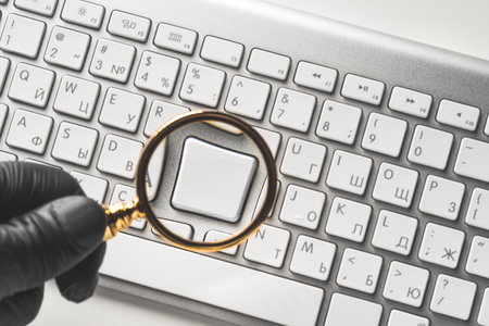 Computer keyboard with one empty white button under magnifier glass in hand in black glove. View directly from aboveの写真素材