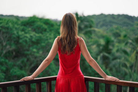 Young woman is standing on balcony in tropical country and look forward on jungleの写真素材