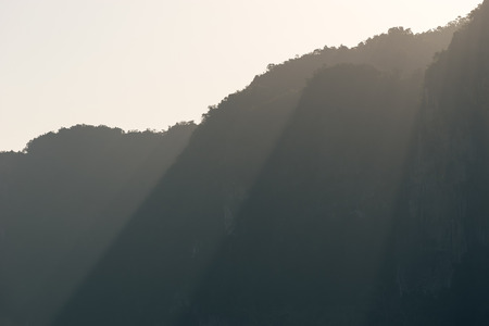 Rays of sunlight fall through peaks of mountains silhouettes in morning hazeの写真素材