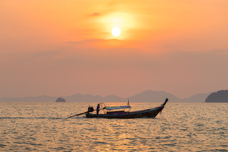 Ao Nang, Krabi Province, Thailand - January 14, 2019: Local fisherman float on thai longtail boat in the sea water at beautiful orange sunsetのeditorial素材