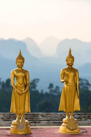 Golden small statues of Buddha in the Wat Tham Suea Tiger cave temple on the background of the silhouettes of the mountains in Thailandの写真素材