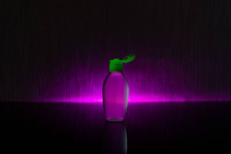 A small bottle of antiseptic liquid sanitizer gel for hands with an open lid on a dark background with a colored glow. Concept photoの写真素材