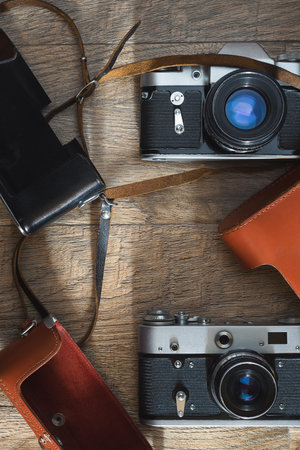 Photographic equipment - old retro film photo cameras and leather cases on wooden background. Flat...