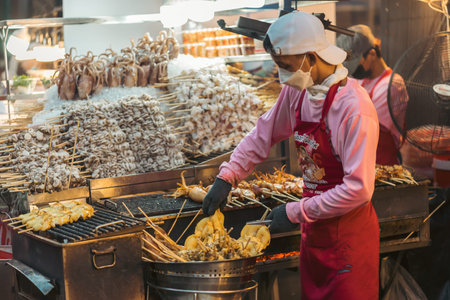 Unidentified Thai man selling grilled squid at street food market in Chinatown district in Bangkok