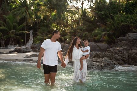 Happy smile european family have rest and run on white sand beach. Father, long black chestnut hair mother, blond baby boy. white cotton clothes. boho dress. t-shorts.Thailand. Aquamarine crystal seaの写真素材