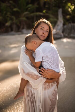 Happy smile european family have rest and run on white sand beach. Father, long black chestnut hair mother, blond baby boy. white cotton clothes. boho dress. t-shorts.Thailand. Aquamarine crystal seaの写真素材