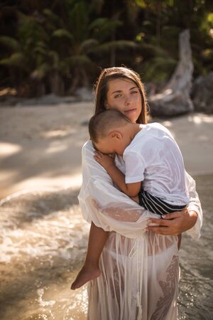 Happy smile european family have rest and run on white sand beach. Father, long black chestnut hair mother, blond baby boy. white cotton clothes. boho dress. t-shorts.Thailand. Aquamarine crystal seaの写真素材