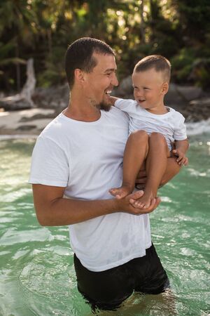 Happy smile european family have rest and run on white sand beach. Father, long black chestnut hair mother, blond baby boy. white cotton clothes. boho dress. t-shorts.Thailand. Aquamarine crystal seaの写真素材