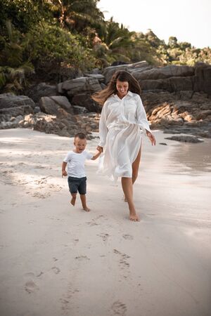 Happy smile european family have rest and run on white sand beach. Father, long black chestnut hair mother, blond baby boy. white cotton clothes. boho dress. t-shorts.Thailand. Aquamarine crystal seaの写真素材