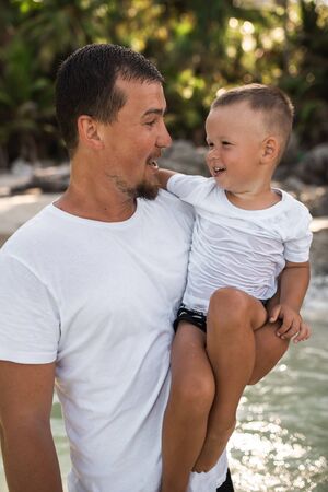 Happy smile european family have rest and run on white sand beach. Father, long black chestnut hair mother, blond baby boy. white cotton clothes. boho dress. t-shorts.Thailand. Aquamarine crystal seaの写真素材