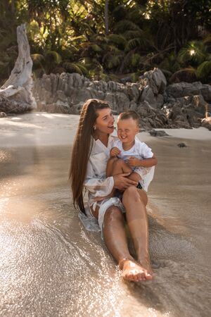 Happy smile european family have rest and run on white sand beach. Father, long black chestnut hair mother, blond baby boy. white cotton clothes. boho dress. t-shorts.Thailand. Aquamarine crystal seaの写真素材