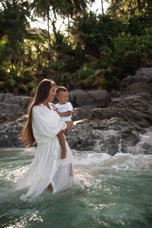 Happy smile european family have rest and run on white sand beach. Father, long black chestnut hair mother, blond baby boy. white cotton clothes. boho dress. t-shorts.Thailand. Aquamarine crystal seaの写真素材