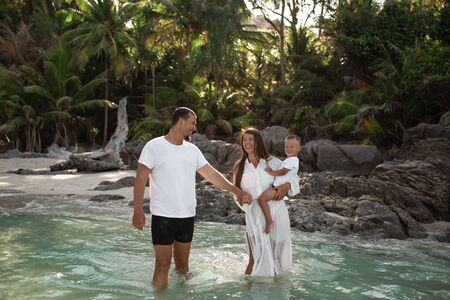 Happy smile european family have rest and run on white sand beach. Father, long black chestnut hair mother, blond baby boy. white cotton clothes. boho dress. t-shorts.Thailand. Aquamarine crystal seaの写真素材