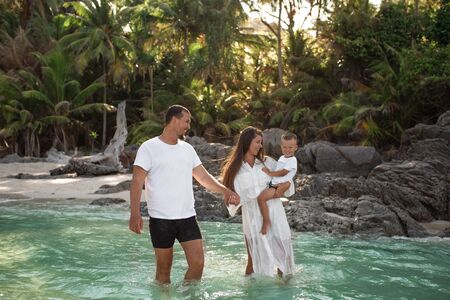 Happy smile european family have rest and run on white sand beach. Father, long black chestnut hair mother, blond baby boy. white cotton clothes. boho dress. t-shorts.Thailand. Aquamarine crystal seaの写真素材