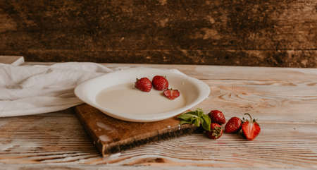 scattered juicy fresh red strawberries on the table with vintage plank. mint leaf. drops and splashes of spilled milk. vegetable cutting board. High quality photoの写真素材