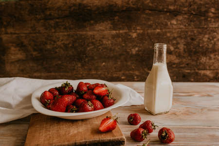scattered juicy fresh red strawberries on the table with vintage plank. mint leaf. drops and splashes of spilled milk. vegetable cutting board. High quality photoの写真素材