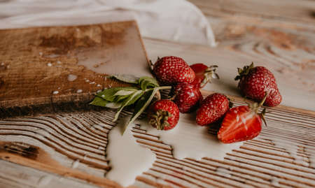 scattered juicy fresh red strawberries on the table with vintage plank. mint leaf. drops and splashes of spilled milk. vegetable cutting board. High quality photoの写真素材