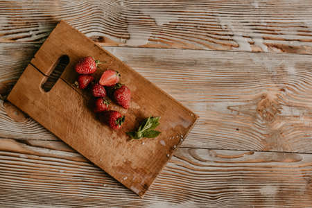 scattered juicy fresh red strawberries on the table with vintage plank. mint leaf. drops and splashes of spilled milk. vegetable cutting board. High quality photoの写真素材
