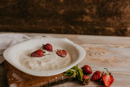 scattered juicy fresh red strawberries on the table with vintage plank. mint leaf. drops and splashes of spilled milk. vegetable cutting board. High quality photoの写真素材