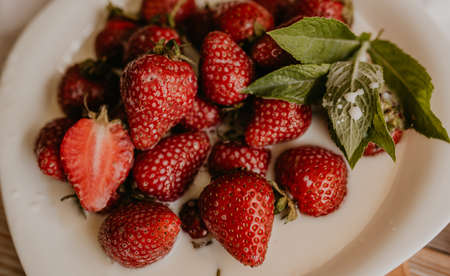scattered juicy fresh red strawberries on the table with vintage plank. mint leaf. drops and splashes of spilled milk. vegetable cutting board. High quality photoの写真素材
